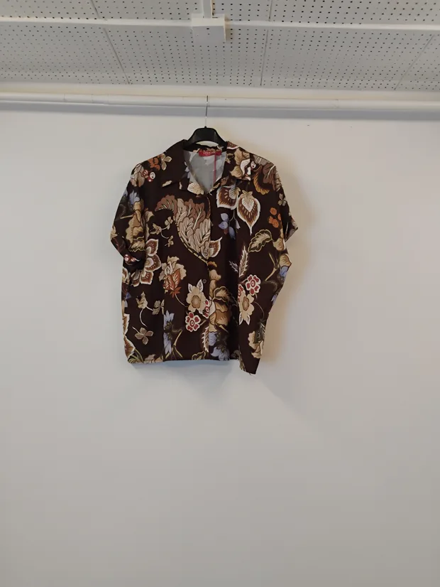 Hanger shot input — a brown floral print short-sleeve blouse hanging against a plain shop wall