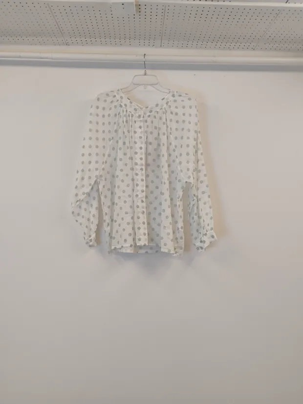 Hanger shot input — a white blouse with a small dotted print and tie neck, hanging against a plain shop wall