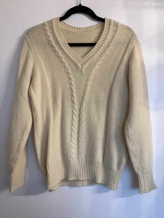 Hanger shot input — a cream cable-knit V-neck jumper on a black hanger against a pale wall