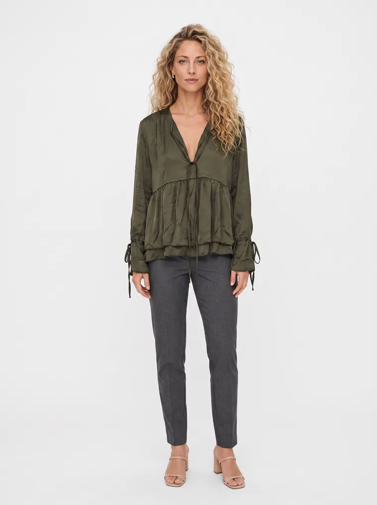 MODA AI output — a woman with curly blonde hair wearing the olive tiered blouse with grey trousers in a clean studio