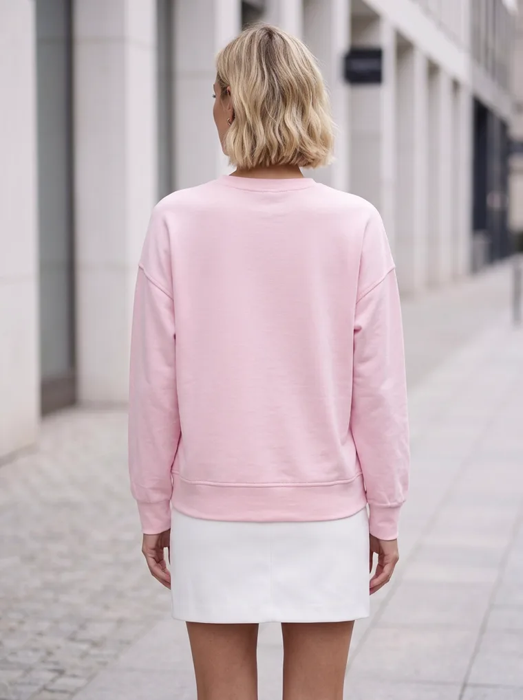 A pale pink sweatshirt with tonal embroidery, a white mini skirt and kitten-heel sandals, on a street lined with stone columns. Embroidered Sweatshirt in pale pink, back view