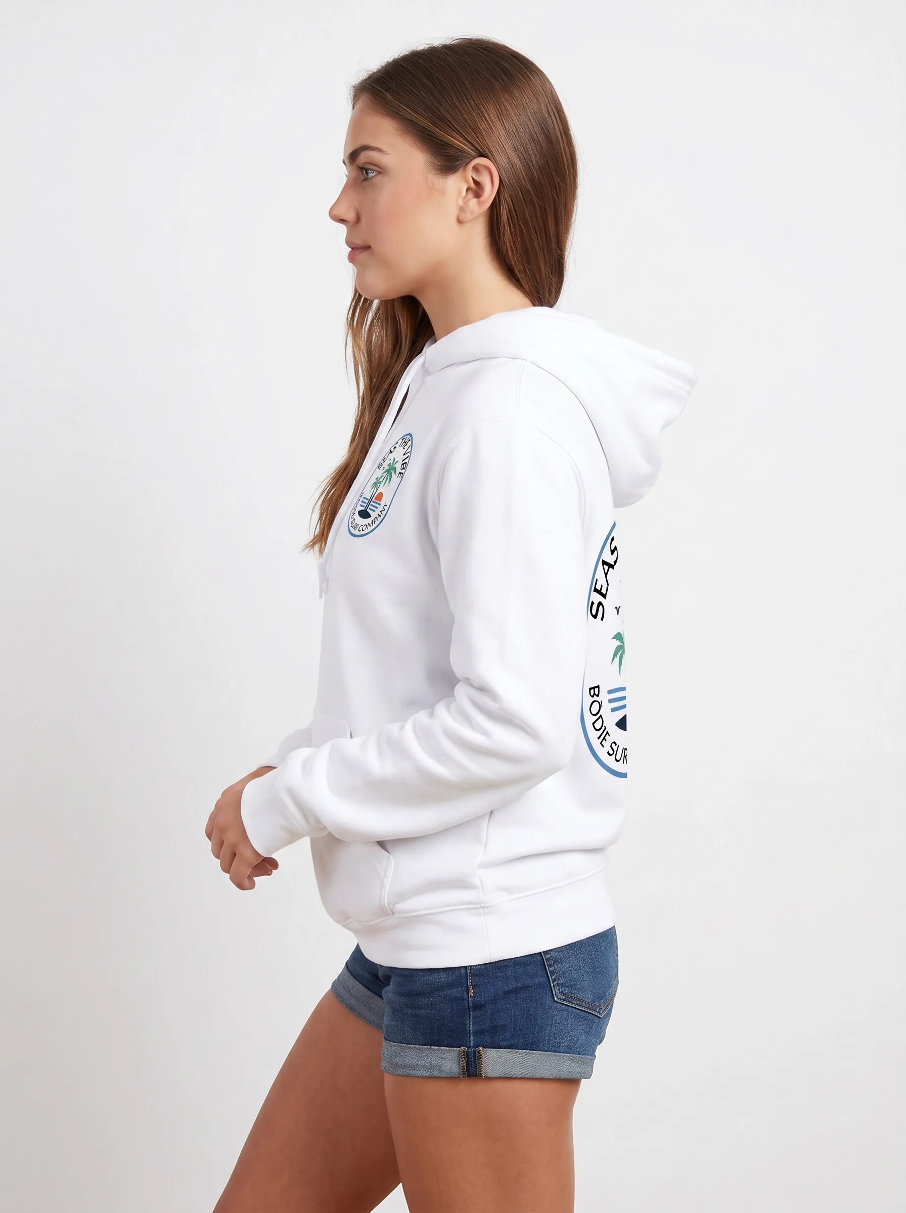 MODA AI side profile — brunette model in white Bödie Surf Company hoodie, full side view showing the Seas the Vibe oval badge on the chest and the matching back logo emerging on the same frame