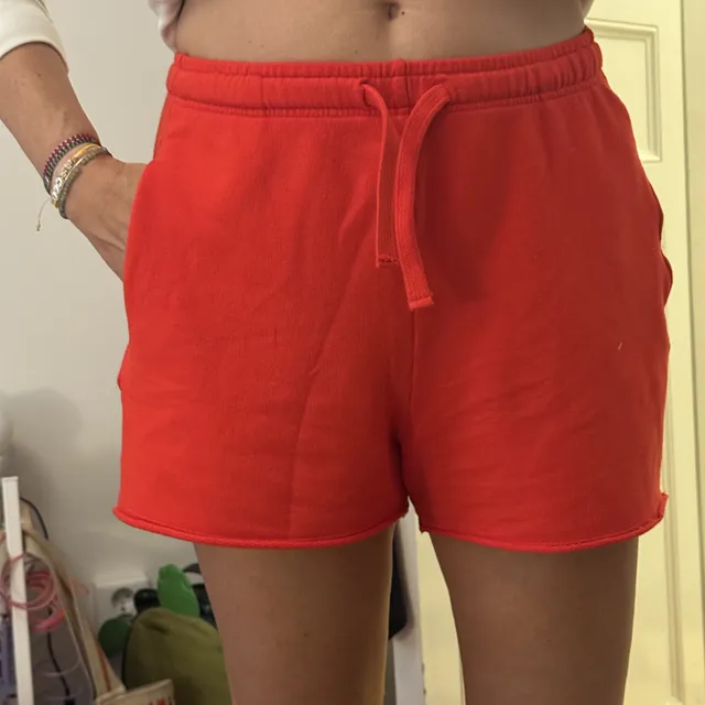 The seller’s phone photo of red drawstring sweat shorts worn by a person and cropped at the waist, against a yellow bedroom wall