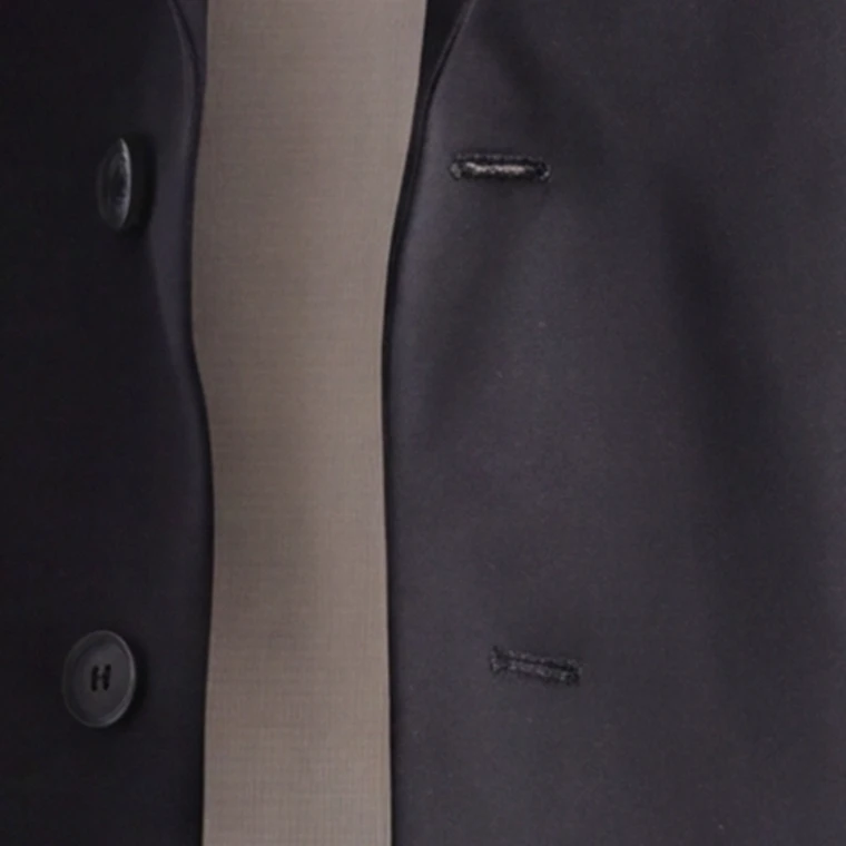 The same square of the black blazer cut directly from the 4K frame, the buttonhole stitching, the button edge and the belt buckle hardware sharply defined