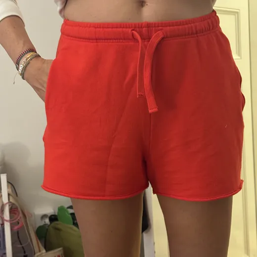 The starting photo for Drawstring Shorts in Red: the shorts worn, cropped at the waist, against a bedroom wall