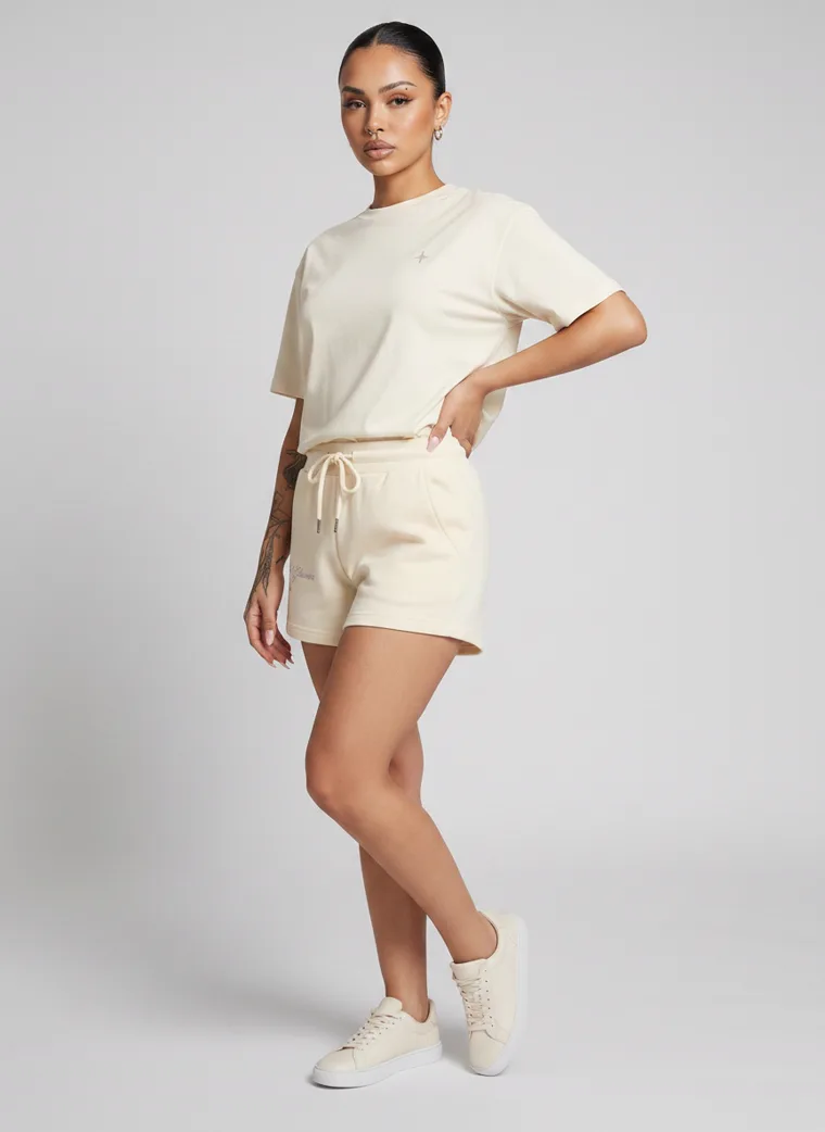 Cream drawstring sweat shorts styled with a matching boxy tee and cream sneakers on pale grey. Drawstring Shorts in Cream, frame 3 of 5