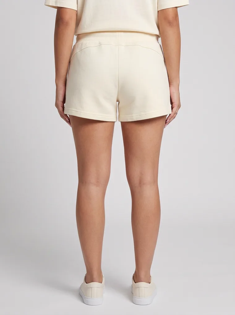 Cream drawstring sweat shorts styled with a matching boxy tee and cream sneakers on pale grey. Drawstring Shorts in Cream, frame 4 of 5