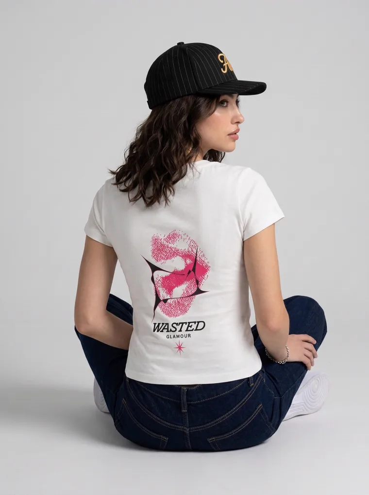 A fitted white tee with a pink lips graphic on the front and a rose print with lettering on the back, worn with dark indigo jeans and a black cap. Graphic Tee in White, frame 2 of 5