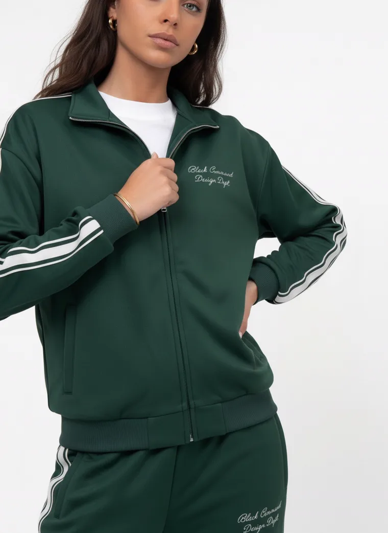 A forest green track jacket and pants with white side stripes and small embroidered chest text on pale grey. Track Jacket and Pants in Forest, frame 2 of 5