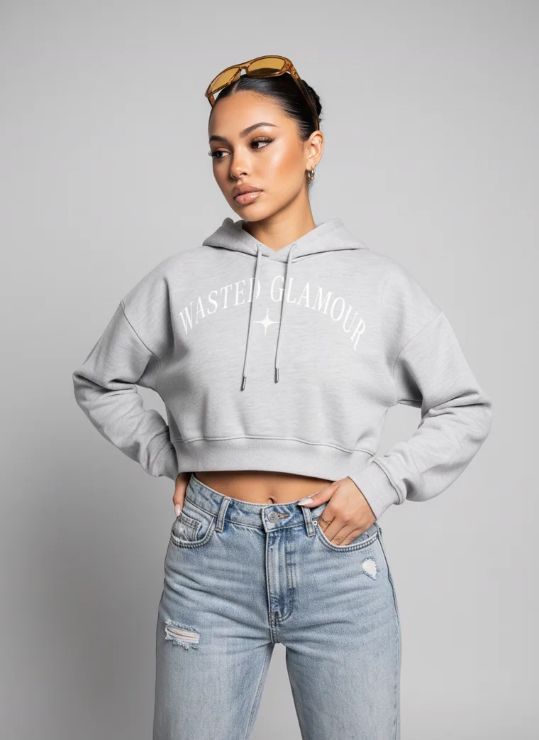 A grey marl cropped hoodie with a small chest print, worn with light wash jeans and sunglasses pushed into the hair. Cropped Hoodie in Grey Marl, frame 1 of 5