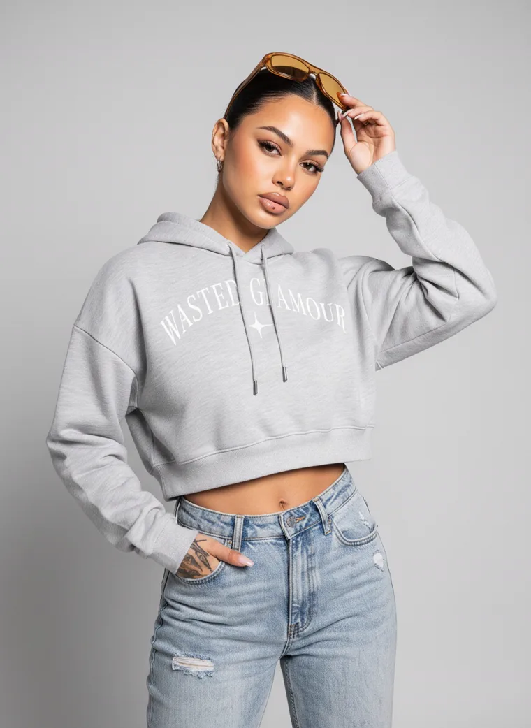 A grey marl cropped hoodie with a small chest print, worn with light wash jeans and sunglasses pushed into the hair. Cropped Hoodie in Grey Marl, frame 2 of 5