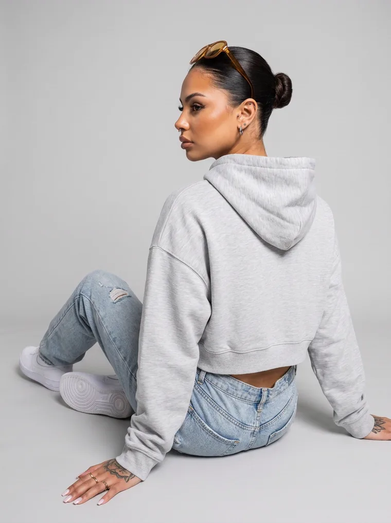A grey marl cropped hoodie with a small chest print, worn with light wash jeans and sunglasses pushed into the hair. Cropped Hoodie in Grey Marl, frame 3 of 5