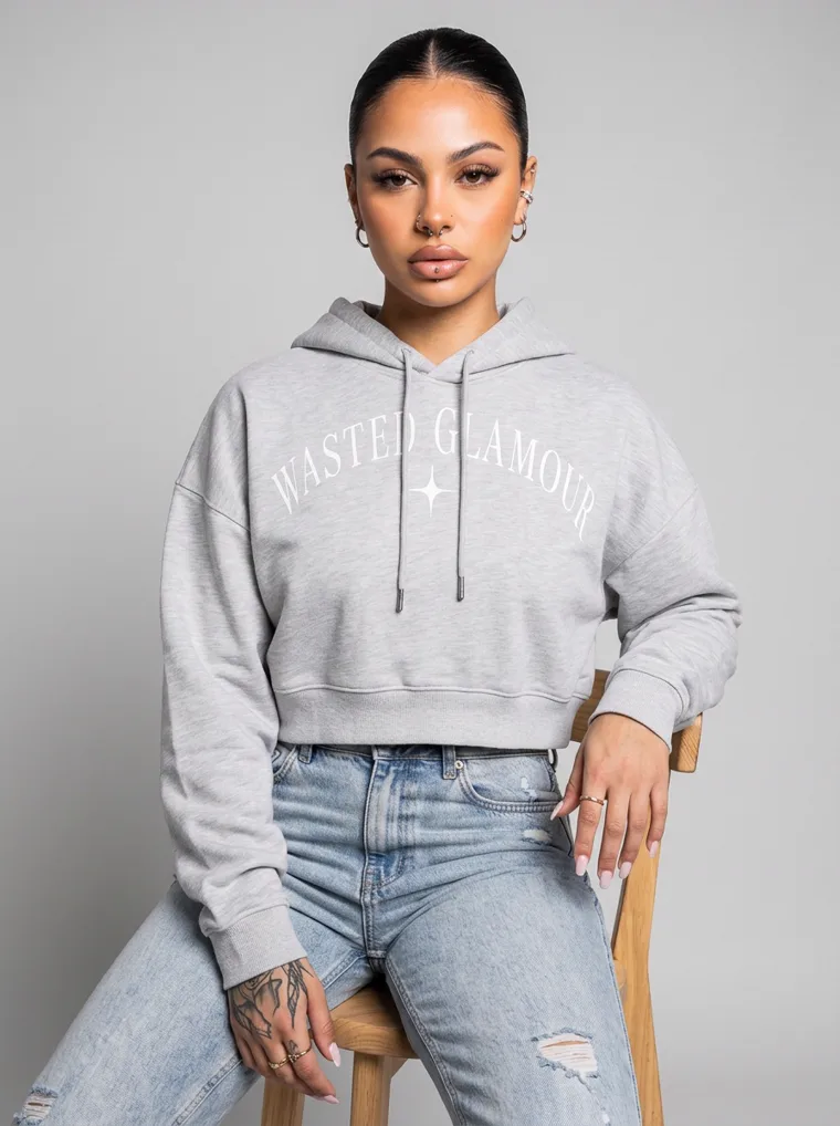 A grey marl cropped hoodie with a small chest print, worn with light wash jeans and sunglasses pushed into the hair. Cropped Hoodie in Grey Marl, frame 4 of 5