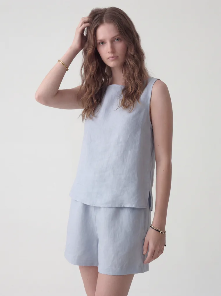 A pale blue linen sleeveless top with matching linen shorts and black flip flops on white. Linen Top and Shorts in Pale Blue, frame 1 of 5