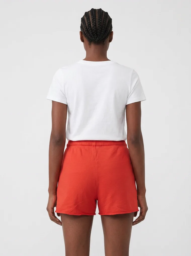Red drawstring sweat shorts styled with a plain white tee and white sneakers on pale grey. Drawstring Shorts in Red, frame 4 of 5