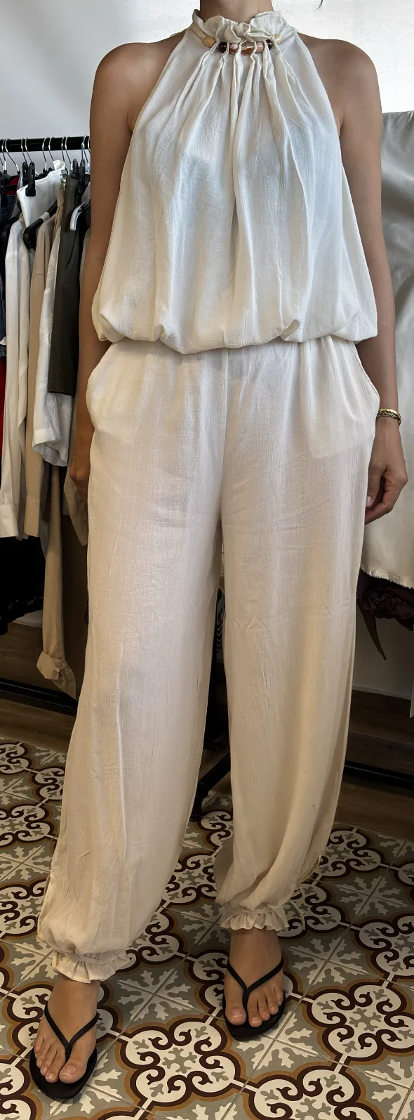 Input photo — a cream halter jumpsuit on a form in a cluttered showroom with a clothing rail behind