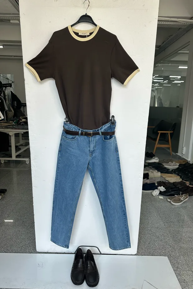 Input photo — a brown ringer tee laid flat with jeans and a belt on a white board in a showroom