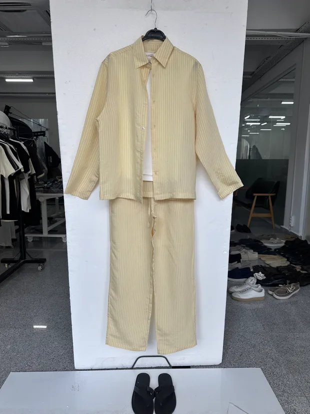 Input photo — a yellow shirt and trousers laid flat on a white board in a showroom