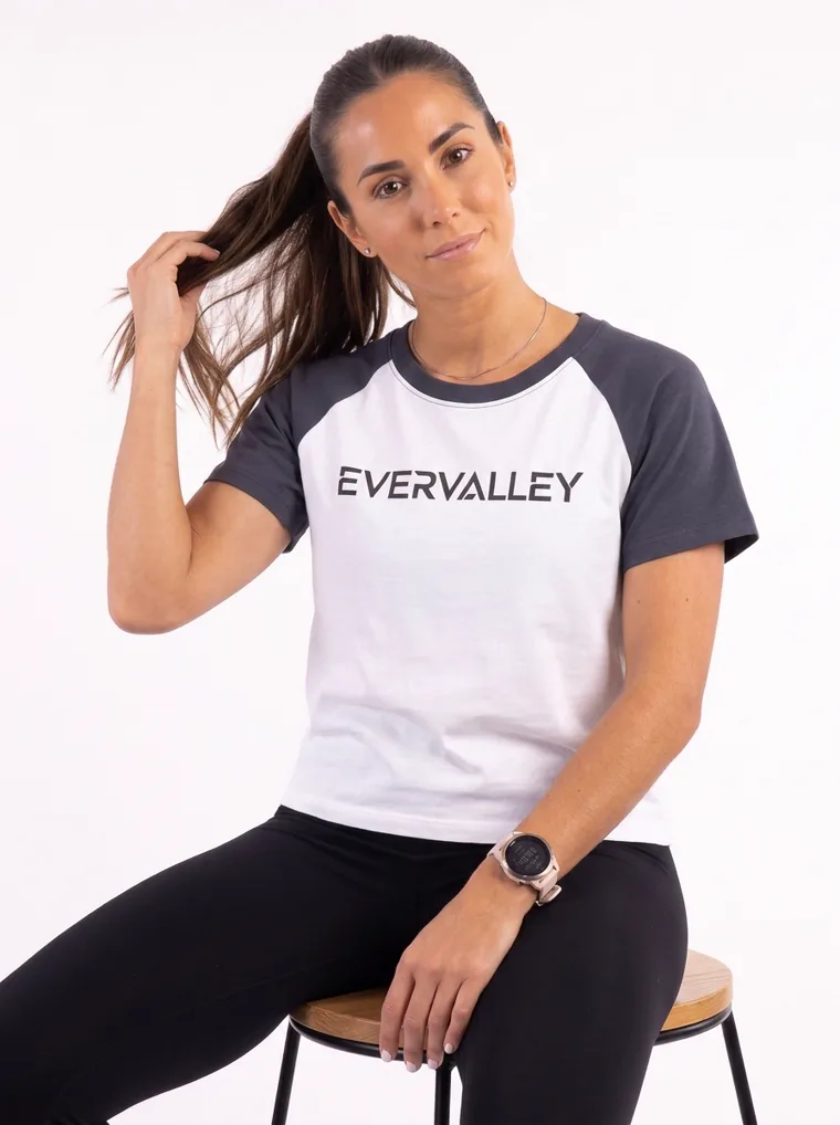 MODA AI output — the raglan tee in navy, seated on a stool, wordmark curving with the chest