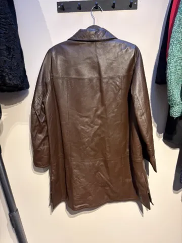 The seller’s phone photo of the brown leather coat on a hanger, back view