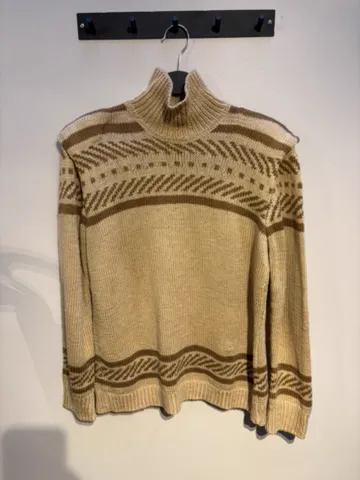 The starting photo for the fair isle mock-neck knit: the Fair Isle knit on a hanger against a shop wall