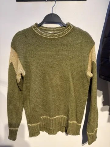 The starting photo for the knit with contrast panels: the olive panelled knit on a hanger against a shop wall