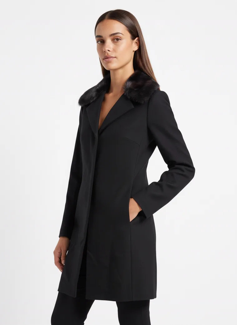 A black single-breasted wool coat with a dark faux-fur collar, worn with black trousers and black boots. Wool Coat with Faux-Fur Collar in black, three-quarter, hands in pockets