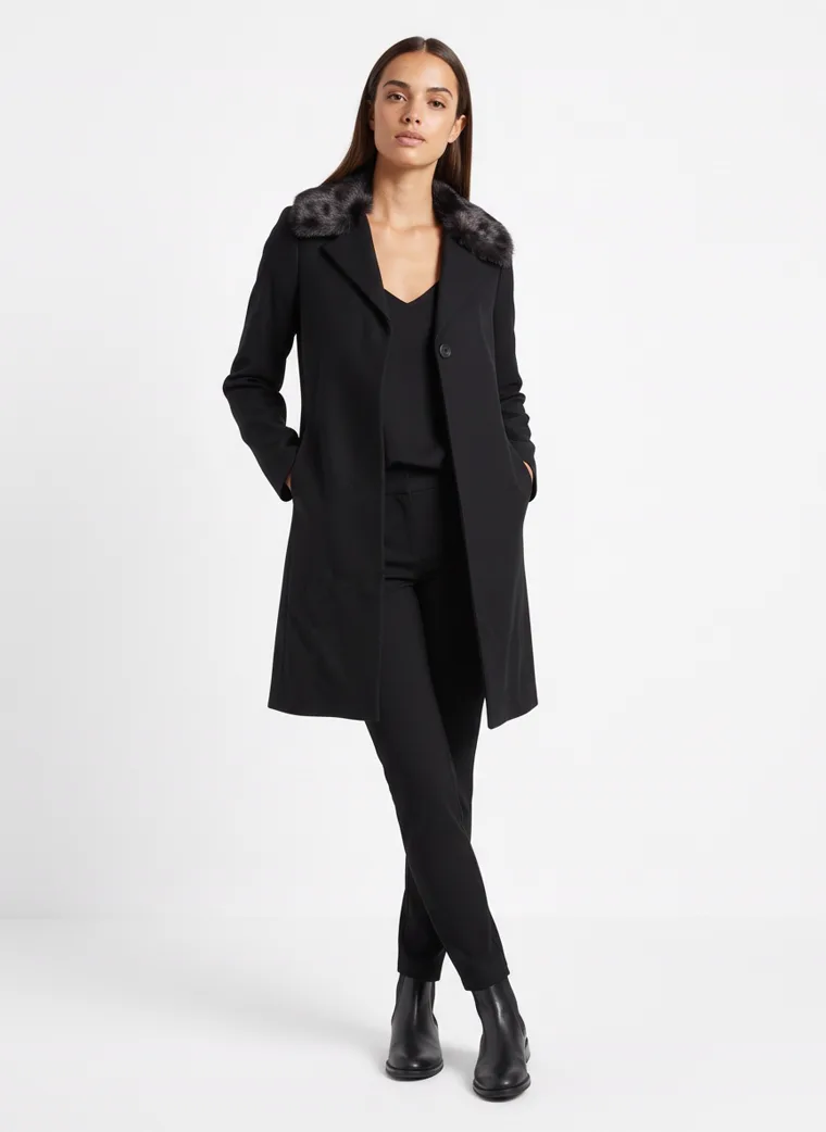 A black single-breasted wool coat with a dark faux-fur collar, worn with black trousers and black boots. Wool Coat with Faux-Fur Collar in black, front, full length