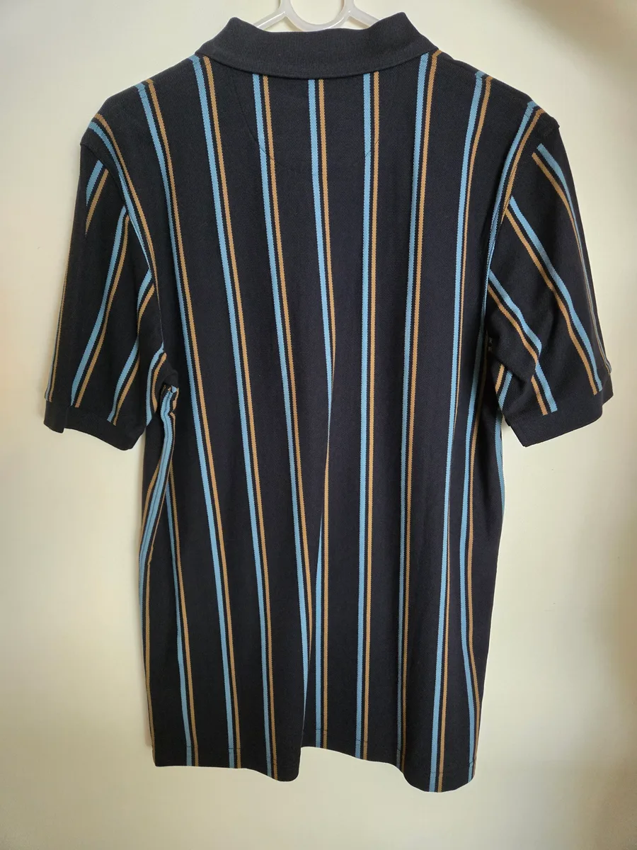 Input hanger shot, back. The same striped navy polo turned around on the hanger, showing the plain back panel, the collar and the short sleeve cuffs