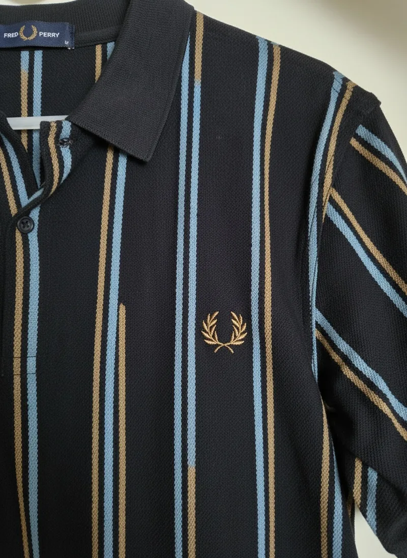 MODA AI shot 10, a macro of the polo collar showing the pique knit texture, the tan and blue stripe edges, the brand neck tab and the embroidered laurel wreath