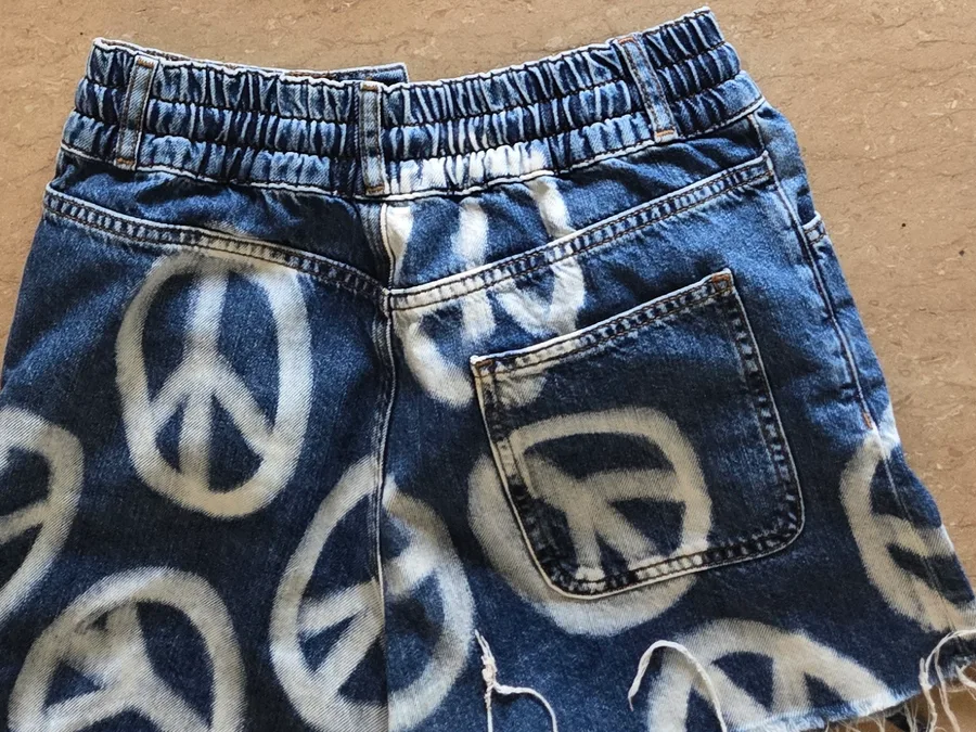 Close crop of the real shorts, back. A wide shirred elastic waistband runs the full width, with a single denim patch pocket on the right and a raw frayed hem