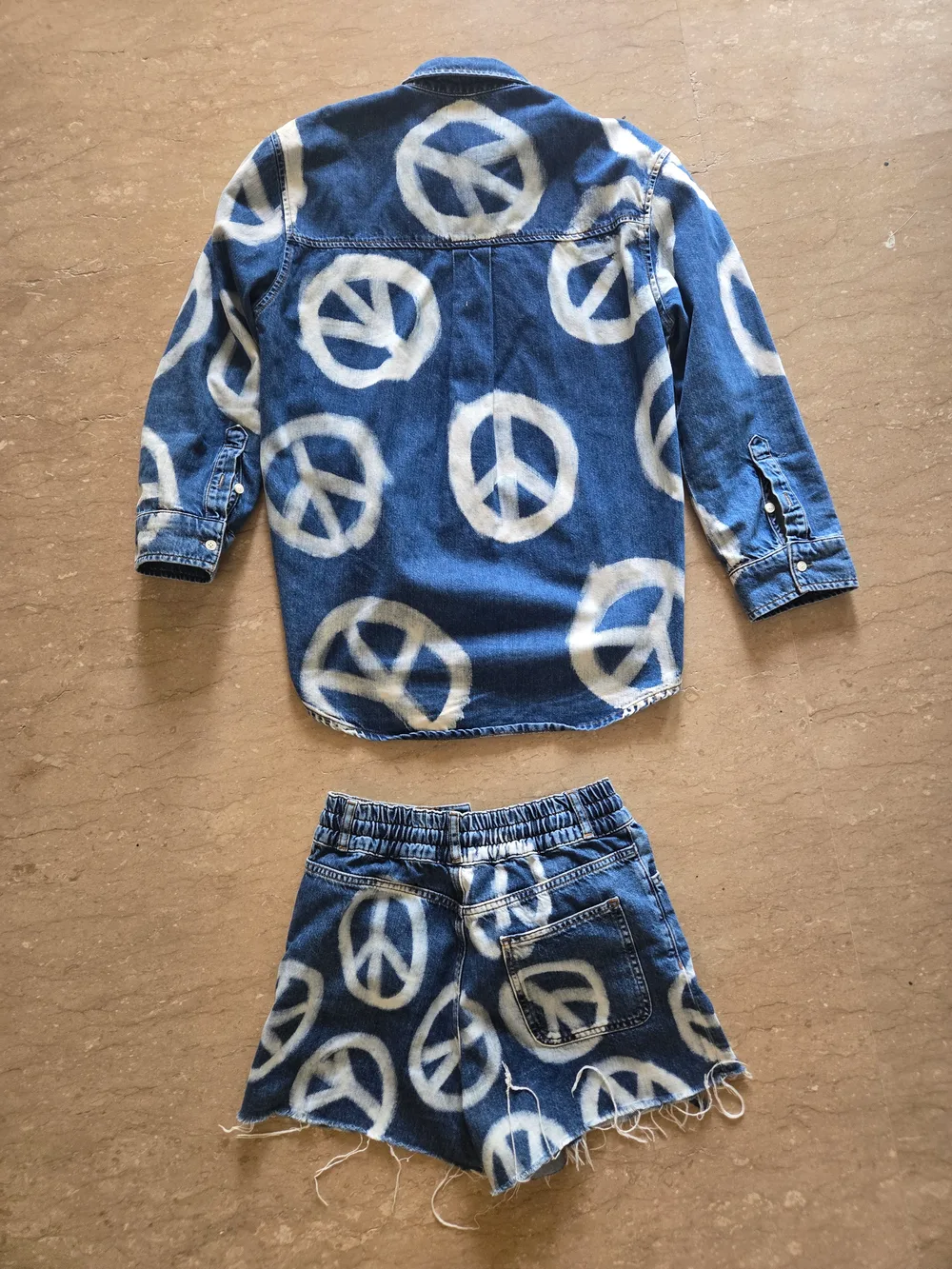 Input flat lay, back. The same denim shirt and shorts turned over, showing the boxy shirt back with its shoulder yoke, and the shorts back with a wide shirred elastic waistband and a single patch pocket on the right